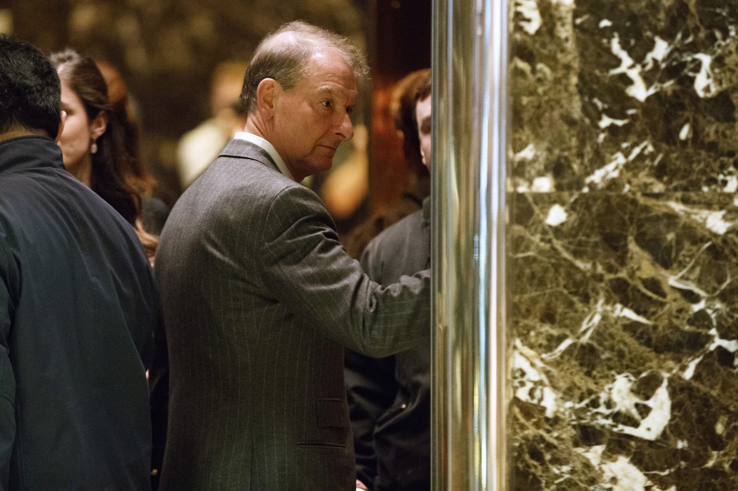 A photo of Paul Atkins in a grey suit, shot through a doorway