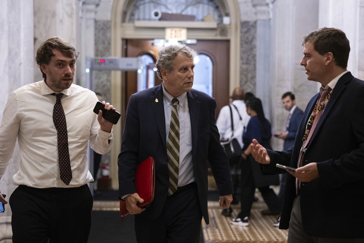 Sherrod brown walking through a government building flanked by two other professionals.