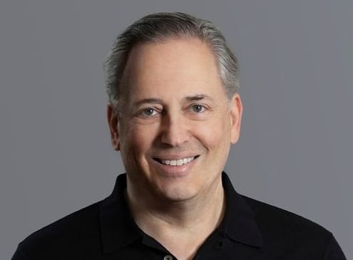 A headshot of David Sacks in a black polo against a grey background