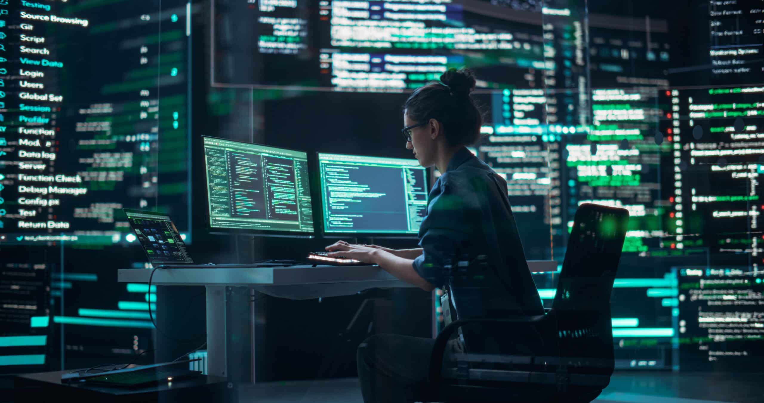 Female Developer Thinking and Typing on Computer, Surrounded by Big Screens Showing Coding Language (Shutterstock)