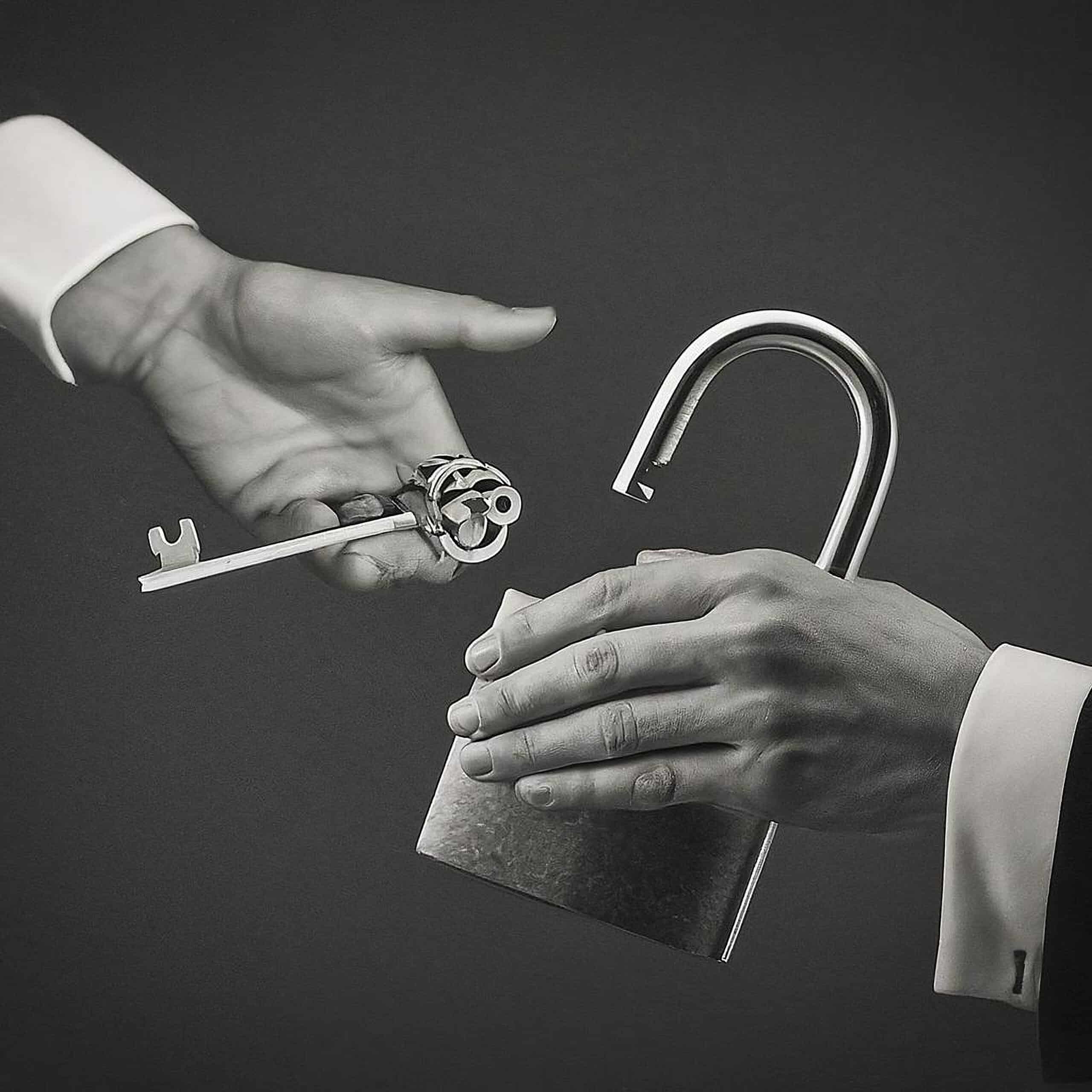 Black and white photo of an open unlock padlock with business shaking hands under it and a key to open the luck of success (Shutterstock)