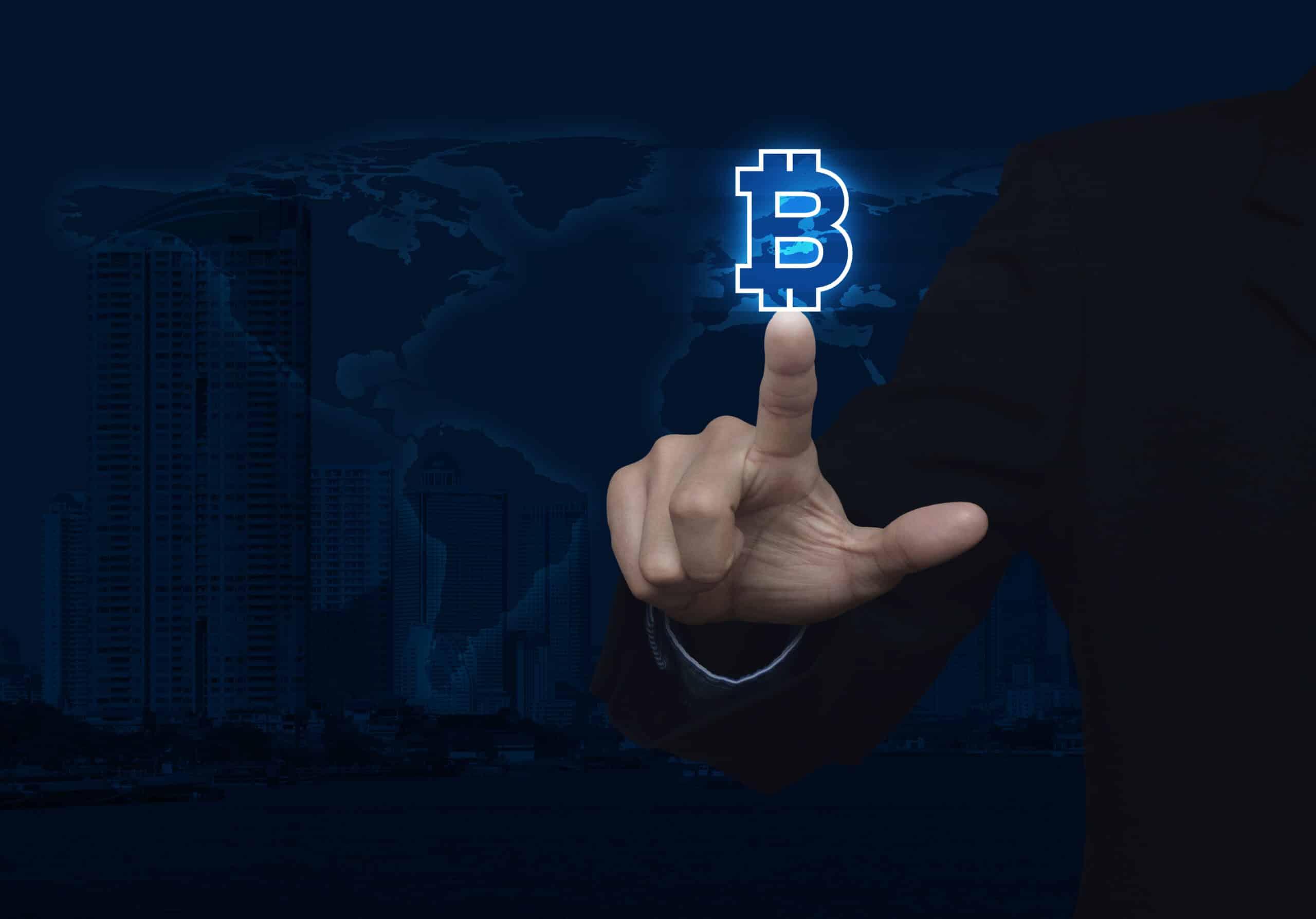 Businessman pressing bitcoin icon over map and city background (Shutterstock)